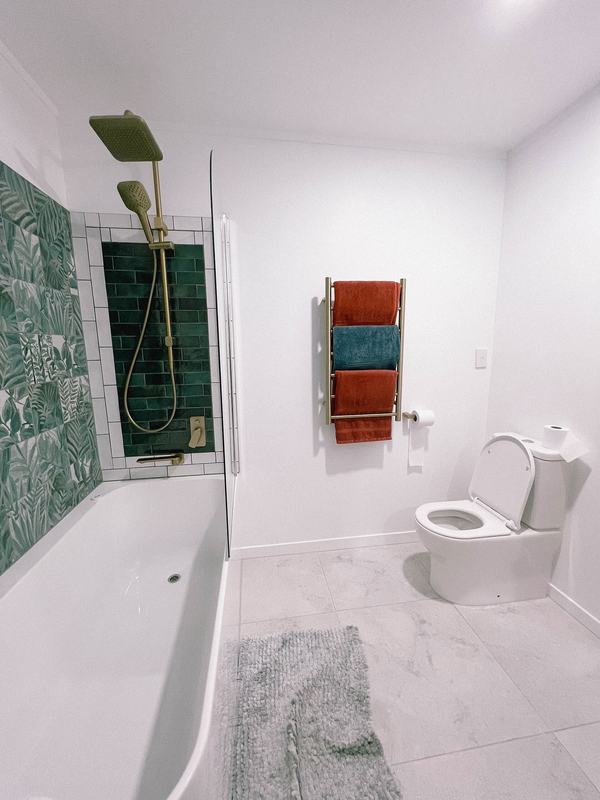 Een vernieuwde badkamer met wit bad, groene wandtegels en een handdoekradiator