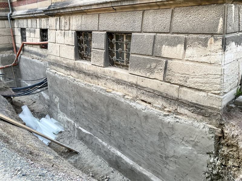 Een keldermuur van natuursteen, uitgegraven aan de buitenkant en bezet met een cementlaag