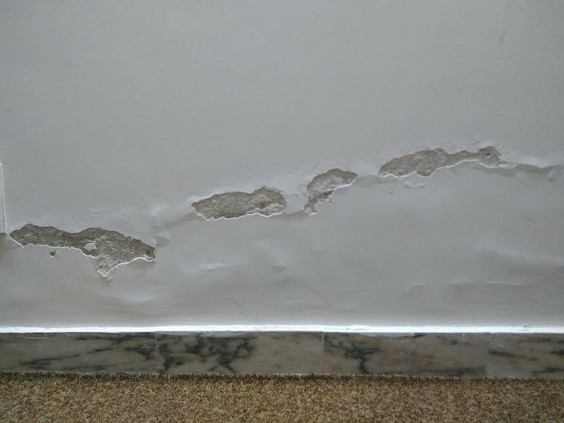 Afgebladderde verf en vochtplekken onderaan een witte binnenmuur